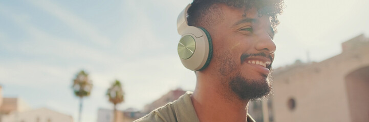 Portrait of young man with beard in an olive-colored shirt listens to music on headphones,...