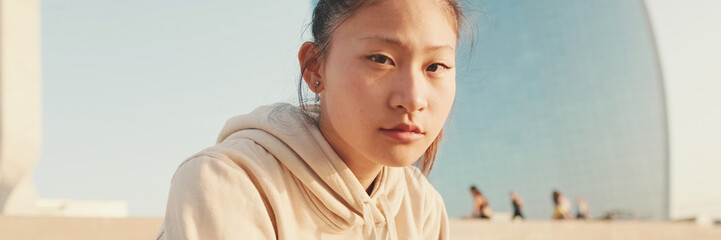 Asian girl in sportswear resting after workout while sitting on steps on modern buildings...