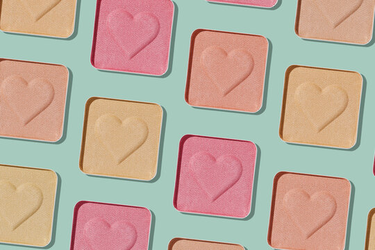 Minimal pattern compact eye shadow glitter swatches on trend green background, pastel color photo, eyeshadow with heart imprint, beige pink colored powder makeup, square pack, cosmetic texture