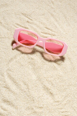 Fototapeta na wymiar Stylish pink colored sunglasses on sand background at sunlight, summer fashion collection eyeglasses with pink glass. Summer romance rose tinted glasses. Top view lifestyle, flat lay