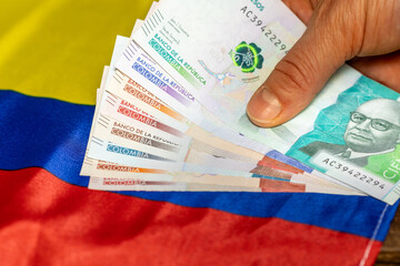 A stack of Colombian pesos held in hand against the background of the flag of Colombia, Business...