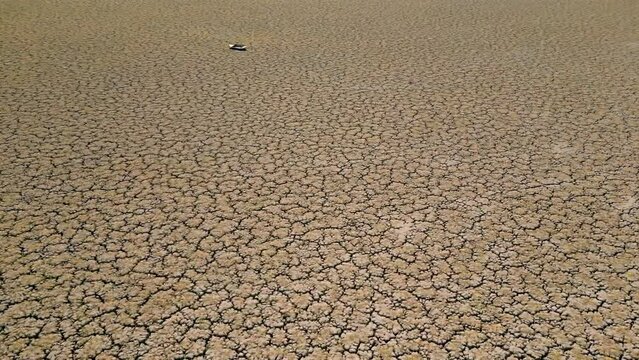 Abandoned row boat on cracked soil on lake bed dried up due to global warming and drought