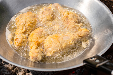 Chicken legs in batter are fried in a wok. Cooking outside