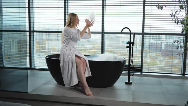 Spa relaxation. Young woman in spa bathrobe sitting at bath with foam in bathtub. Girl relaxing in bathroom at home. Female spending morning in bathroom. Beauty treatment body skin care concept