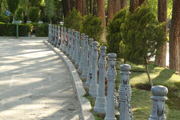 Sunlit trees and greenery create a peaceful oasis in a bustling Isfahan park. A metal fence...