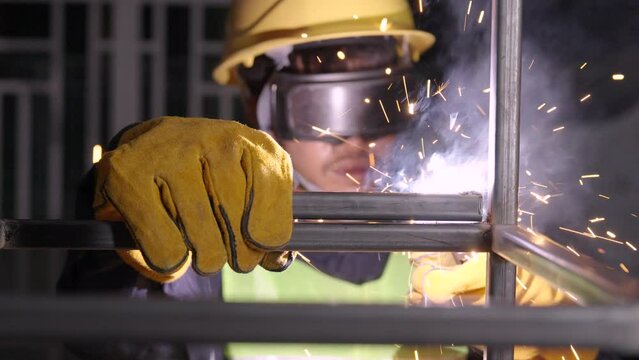 Asian worker wearing safety suit uses a welding machine. The sparking of the welding wire and steel creates sparks.