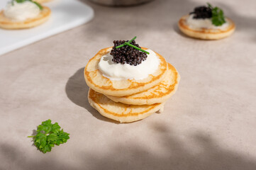 Black caviar with sour cream on a stack of mini blinis or pancakes.