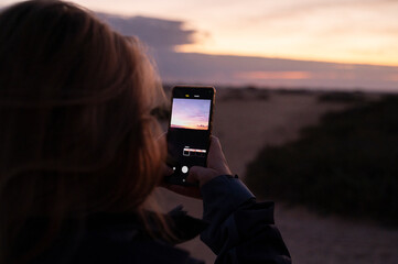 eine person fotografiert mit dem smartphone den sonnenaufgang in den dünen von corralejo auf fuerteventura auf den kanarischen inseln von spanien - obrazy, fototapety, plakaty