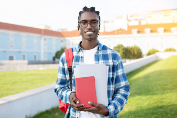 Portrait of smiling black guy with backpack and workbooks outdoors
