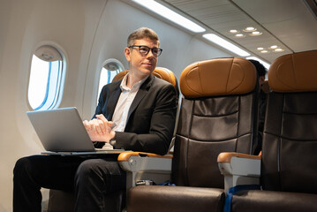 Businessman working with laptop while sitting in airplane seat. Business work and travel concept.
