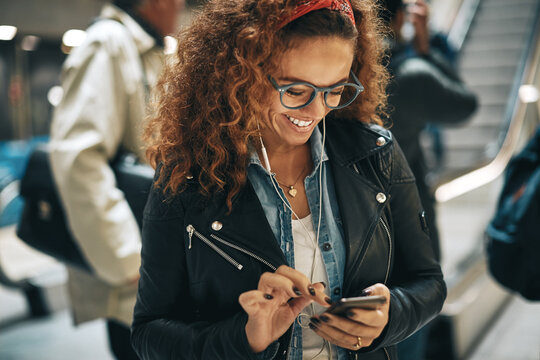 Smiling woman with glasses sending a text while waiting for her train