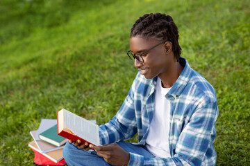 Fototapeta premium black man wearing glasses happily reads book relaxing in park