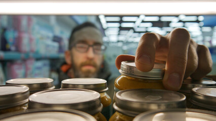Close-up of many baby puree jars on the shelf of a baby goods department and a male buyer takes one