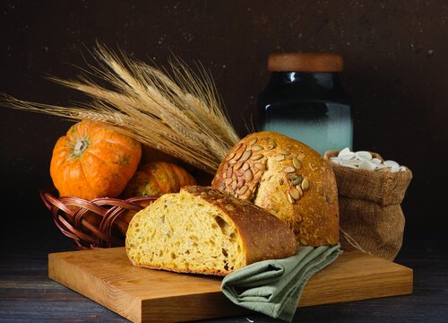 Still life with a loaf of pumpkin bread, spikelets, decorative pumpkins and a wooden board. World Bread Day.