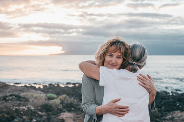 Fototapeta na wymiar Romantic senior couple of women embrace each other on the seashore at sunset light, two embraced people stay together expressing love and tenderness