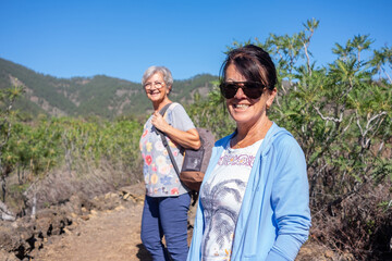 Portrait of happy smiling senior couple of women walking in mountain enjoying healthy living in outdoors. Blue sky