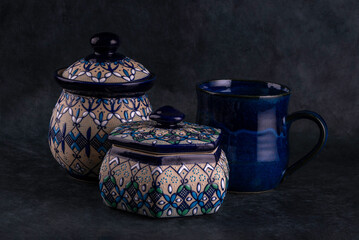 Colorful traditional Mexican clay pots and blue tea cup on a dark background. - 727953926