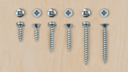 Closeup of different sized screws on a wooden background.