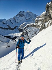Fototapeta na wymiar Younger climbs up the mountain on skis. Ski tourer climbs a large mountain in winter. Ski mountaineering in Braunwald Glarus. High quality photo