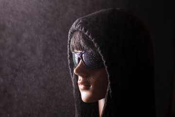 Plastic woman mannequin with black hair wearing a black hoodie and dark sunglasses posing on a...