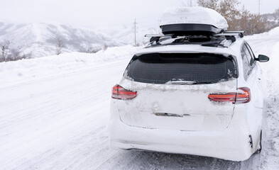a white car in the snow with a roof rack stands on the edge of a snowy road in winter
