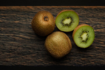 Whole and cut kiwi on a wooden brown table.