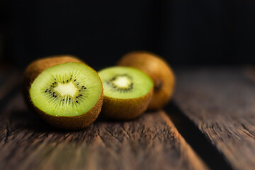 Whole and cut kiwi on a wooden brown table.