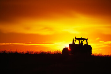 Fototapeta premium Harvest Harmony: High-Contrast Silhouette of a Farm Tractor at Sunrise