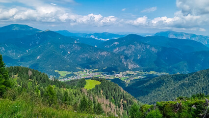 Fototapeta na wymiar Aerial view of Tarvisio and Camporosso in valley Valcanale seen from observation point of Monte Lussari, Friuli Venezia Giulia, Italy. Looking at lush green alpine landscape of hills and meadows