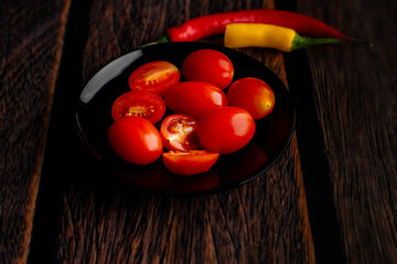 Cherry tomatoes, red and yellow peppers on a black round plate.