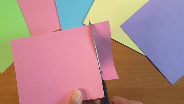 Cutting paper with scissors close-up. Female hands with scissors and pink cardboard. Paper crafts at home. View from above.
