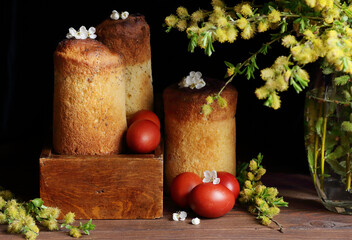 Homemade easter cakes with spring flowers, fresh willow bouquet and red eggs on dark moody rustic...
