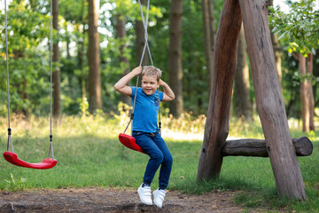 Cheerful happy child playing on entwined rope swing in sunny pine forest during summer