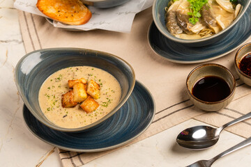 Three bowls of food are on a table, each with a different type of soup. The table is set with a fork, spoon, and knife, and there is a small ball on the table. Scene is casual and inviting