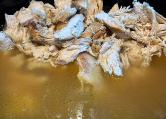Shredded, cooked chicken being added to chicken stock to begin making chicken soup