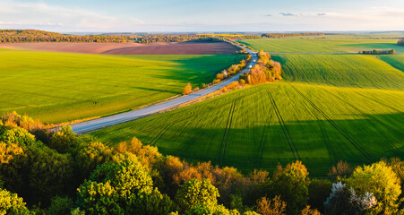 From a bird's eye view, the road passes through farmland and green fields. - obrazy, fototapety, plakaty