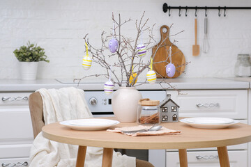 Home spring easter design in kitchen. Plate with cookies on round wooden table, creamic vase with...