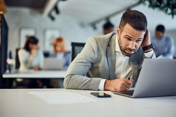 A businessman having thoughts about his new business, working over the laptop, at the office, surrounded by his colleagues.