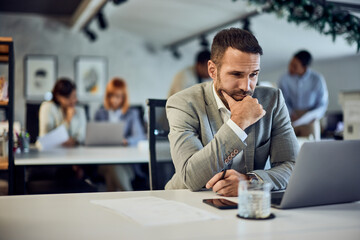 A businessman planning some new ideas, working over the laptop, at the office. His colleagues sitting in the background.