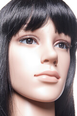 Plastic woman mannequin closeup with black long hair posing on a white background in a high key setup