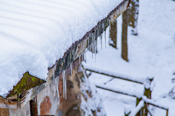 Fototapeta premium Icicles Hanging From A Roof. Roof Icicles. Spring Melting Snow. Snow Melt Roof. Moss Roof Winter. End of Winter.