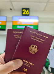 A hand holds two German passports in front of a soft travel airport background on vacation.