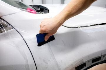 Worker applies a protective film or anti-gravity protective coating to the car headlight. Details of the car white.