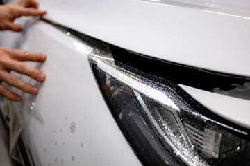 Worker applies a protective film or anti-gravity protective coating to the car headlight. Details of the car white.