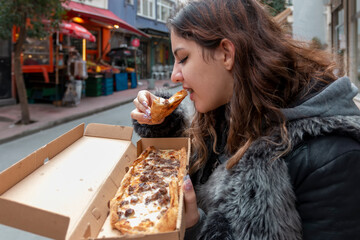 A young beautiful woman eating a piece of pizza in a box.