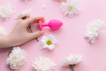 Top view woman hand and bung on pink background with flowers. Concept erotic sex toy for female