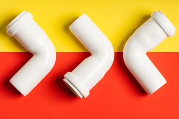 White sewage fittings lying on a colorful bright yellow-red background