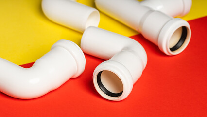 White sewage fittings lying on a colorful bright yellow-red background