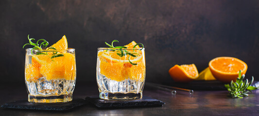 Carbonated cocktail with orange, ice and rosemary in glasses web banner