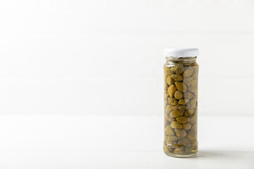 Capers in a glass jar on a wooden kitchen table. Capers with sea salt and rosemary. Pickled capers.Mediterranean cuisine ingredient. Organic spices and seasonings. Copy space.